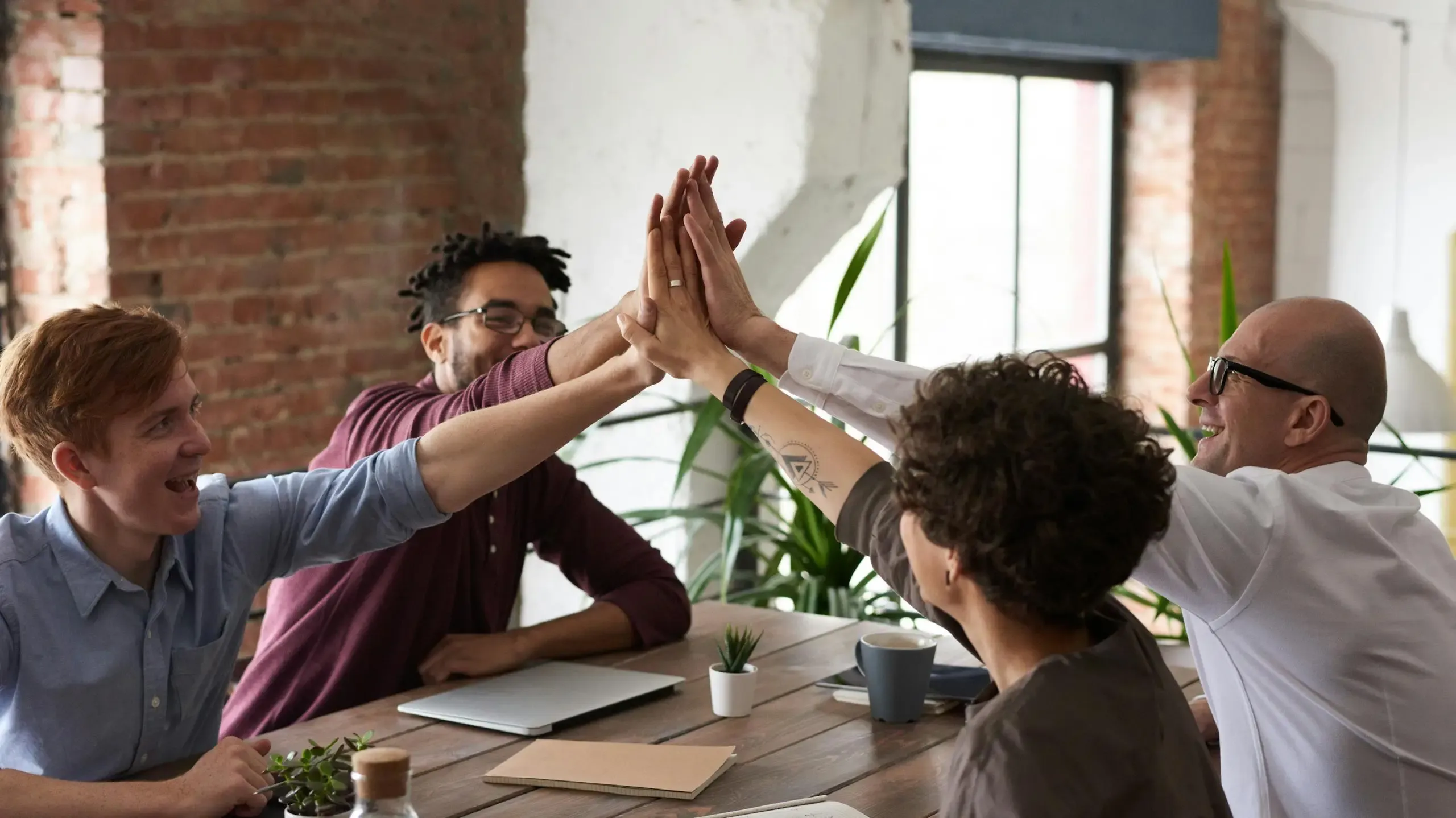 Five colleagues enthusiastically giving high fives to each other during a meeting, celebrating a successful collaboration